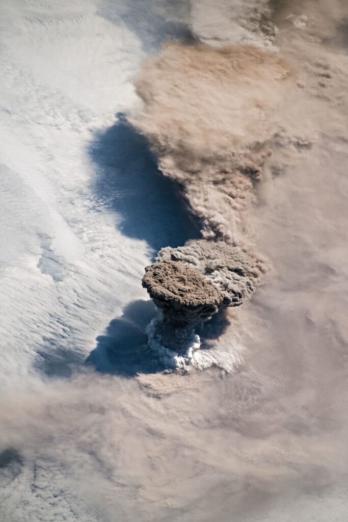 island volcano with ash cloud above dark lava fields reaching the sea
